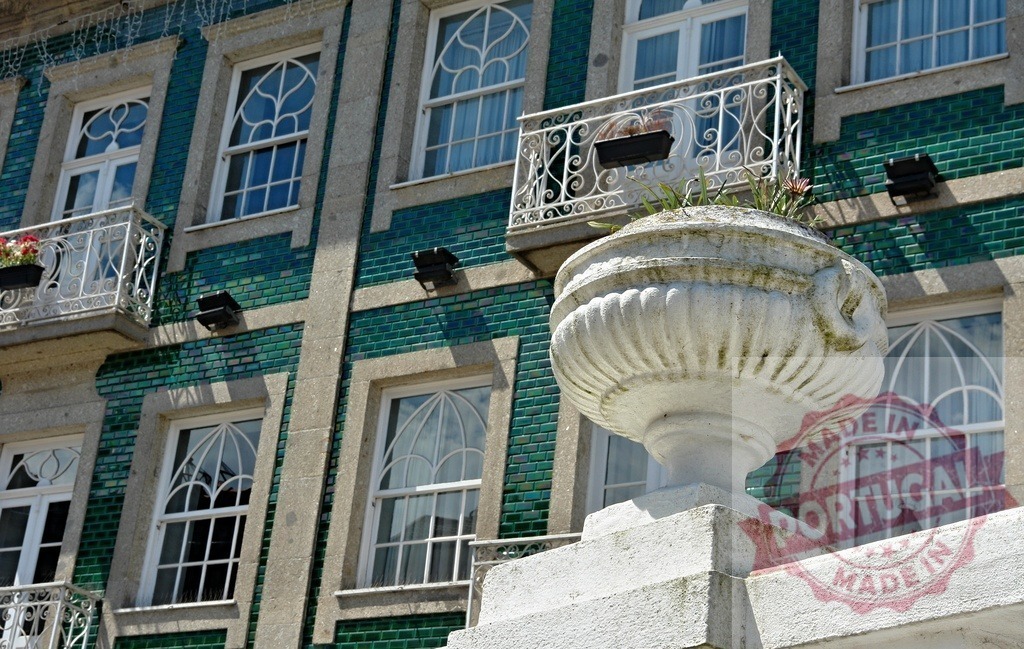Ornamental urn in front of traditional tiled building facade. Region Norte - Portugal | Ornamental stone urn on a balcony with a green tiled building facade and patterned windows - Realisiert mit Pictrs.com