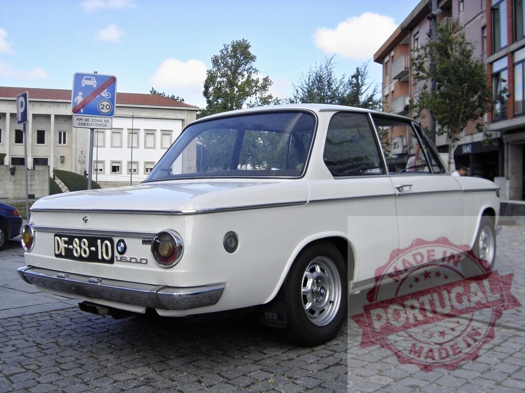 White BMW 1600 parked on cobblestone street in urban setting | Classic white BMW 1600 parked on a cobblestone street, showcasing its vintage design against an urban backdrop - Realisiert mit Pictrs.com