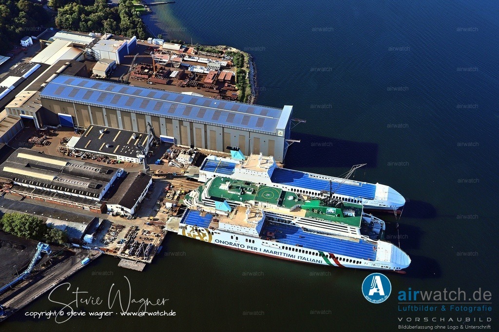 Luftbild Flensburger Schiffbau Gesellschaft - FSG | Im Ersten Weltkrieg konzentrierte sich die Produktion vieler deutscher Werften, einschließlich der FSG, verstärkt auf den Bau von Versorgungsschiffen, Minensuchern und anderen Hilfsschiffen für die Kaiserliche Marine. Konkrete Bauprojekte der FSG aus dieser Zeit umfassten unter anderem Kleinschiffe und Transporteinheiten, die im Rahmen der kriegsbedingten Seeverkehrssicherung eingesetzt wurden.Die Werft in Flensburg an der Förde behielt trotz kriegsbedingter Material- und Personalengpässe ihre operative Bedeutung bei und trug zur maritimen Infrastruktur des Deutschen Reiches bei.