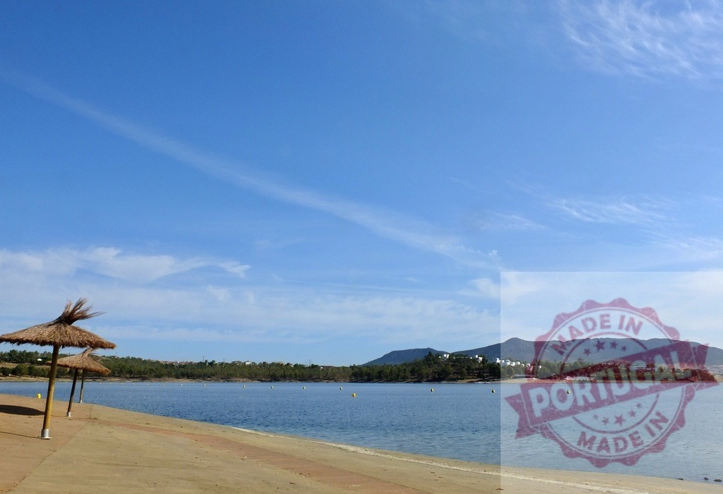 Straw beach umbrellas lining tranquil seaside resort landscape. Spain - Extremadura | Straw umbrellas providing shade on a peaceful beach with blue water and distant mountains - Realisiert mit Pictrs.com
