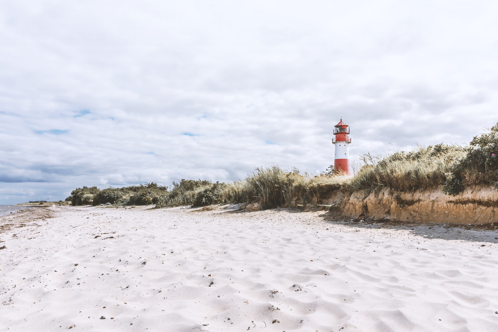 XXL Wandbild: Leuchtturm am Sandstrand | Spüre den feinen Sand unter den Füßen und den weiten Blick über die Küste. Dieses XXL Wandbild rückt den ikonischen rot-weißen Leuchtturm Falshöft in eine weitläufige Strandlandschaft, die Ruhe und Beständigkeit ausstrahlt. Die helle, natürliche Farbgebung des Strandes harmoniert perfekt mit dem weiten Himmel und schafft eine Atmosphäre von Freiheit und Klarheit in jedem Raum.Um die volle Wirkung dieser Szenerie auszuschöpfen, ist das Motiv in beeindruckenden Abmessungen von bis zu 180 x 120 cm erhältlich. Damit ist es die ideale Wahl, um große Wandflächen in Wohnzimmern, Hotels oder repräsentativen Büros stilvoll zu beleben.