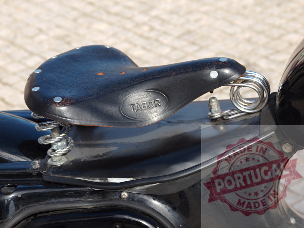 Vintage Tabor leather saddle on classic motorcycle | Black leather seat with springs, rivets, and Tabor brand on a classic motorcycle - Realized with Pictrs.com