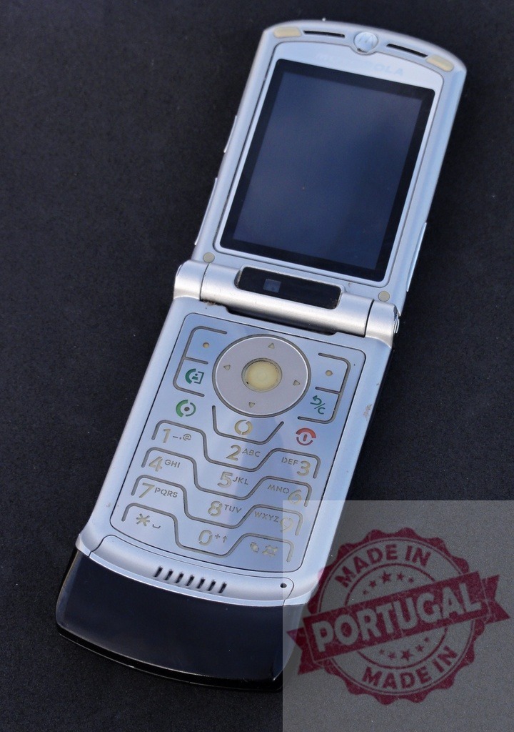 Motorola Razr V3 flip phone showing blank screen on dark background | Old-fashioned silver Motorola Razr V3 mobile phone lying open on a dark background, displaying a blank screen - Realisiert mit Pictrs.com