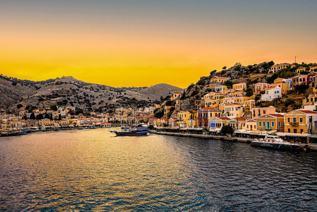 Sonnenuntergang über dem malerischen Hafen der griechischen Insel Symi bei Rhodos | Das Bild zeigt den malerischen Hafen von Symi (Gialos) auf der gleichnamigen griechischen Insel in der Ägäis, die für ihre bunten neoklassizistischen Häuser bekannt ist.Highlights der Insel Gialos und Chorio: Der lebendige Hafenbereich (Gialos) und das historische Oberdorf (Chorio) laden zum Erkunden der engen Gassen ein.Kloster Panormitis: Das berühmte erzengel-michael-Kloster im Süden der Insel ist ein beliebtes Ausflugsziel. Traumhafte Buchten: Viele ruhige Strände wie die St. George’s Bay sind am besten mit dem Boot erreichbar. - Realisiert mit Pictrs.com