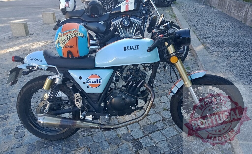 Bullit Spirit 125 motorcycle parked on cobblestone street | Stylish Bullit Spirit 125 motorcycle with Gulf livery parked on a cobblestone street, showcasing its classic design and branding - Realisiert mit Pictrs.com