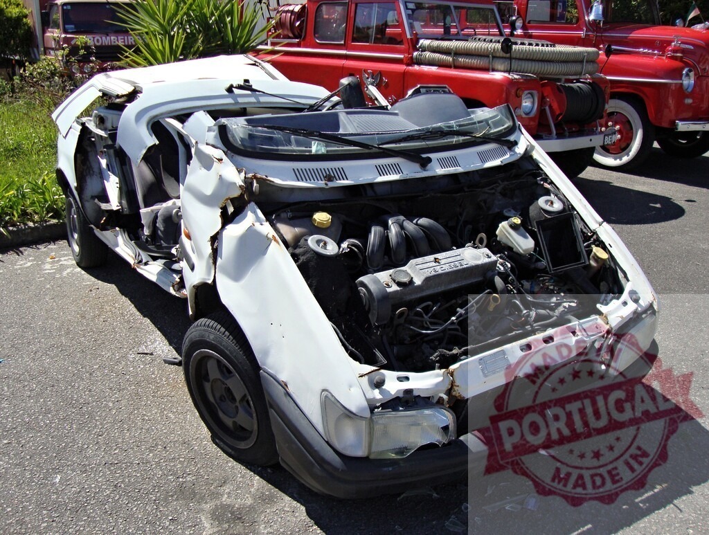 Wrecked white car showing engine and interior after crash near firetruck | Totaled white car with visible engine and interior, parked near a firetruck, illustrating a serious road accident - Realisiert mit Pictrs.com