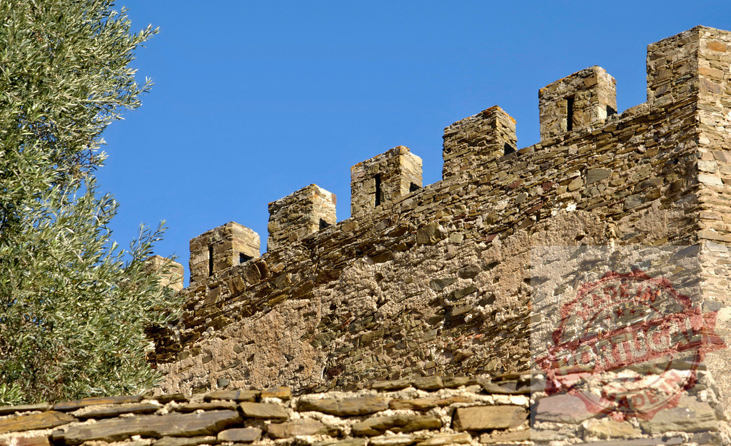 Medieval castle battlements protecting ancient stone wall | Castle wall with merlons and crenels under a clear blue sky, showing historical defense - Realisiert mit Pictrs.com
