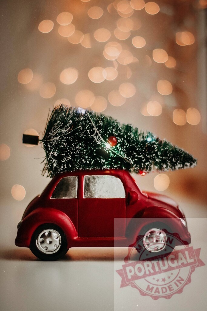 Red toy car carrying christmas tree on roof with bokeh lights in background | Miniature red car transporting christmas tree on its roof against bokeh effect lights, celebrating christmas holidays - Realisiert mit Pictrs.com