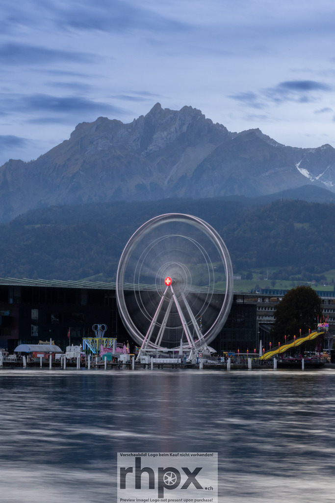 Riesenrad Luzern mit Pilatus im Hintergrund | Bewegung. Fels. Tradition.Das drehende Riesenrad der Luzerner Määs verschmilzt in dieser Aufnahme zu einem dynamischen Kreis vor der ewigen Ruhe des Pilatus. Ein faszinierender Kontrast zwischen flüchtigem Festmoment und majestätischer Bergwelt am Seeufer.Wähle unter "Produktauswahl" dein Wunschformat: Vom klassischen Wandbild über Puzzle &amp; Tassen bis zum digitalen Download (z.B. als Handy-Hintergrund). - Realisiert mit Pictrs.com
