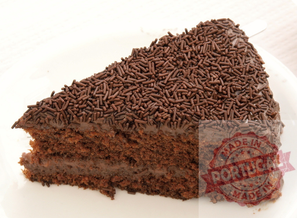 Chocolate cake slice with chocolate sprinkles on top | Chocolate cake slice displaying rich layers, ganache filling, and delicious sprinkles - Realisiert mit Pictrs.com