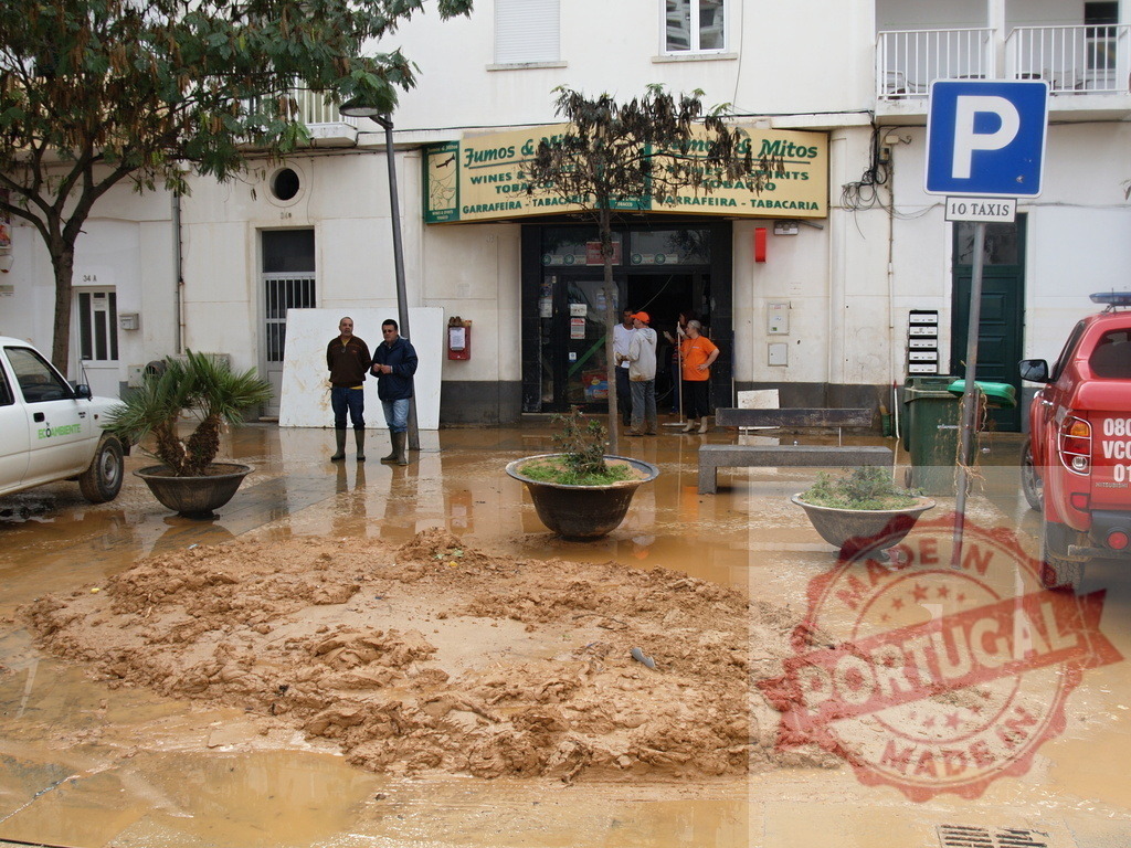 Flood aftermath with mud and people cleaning street | Albufeira Flood - discruction by weather problems Urban street covered in mud and floodwater after a natural disaster, impacting a local shop - Realized with Pictrs.com