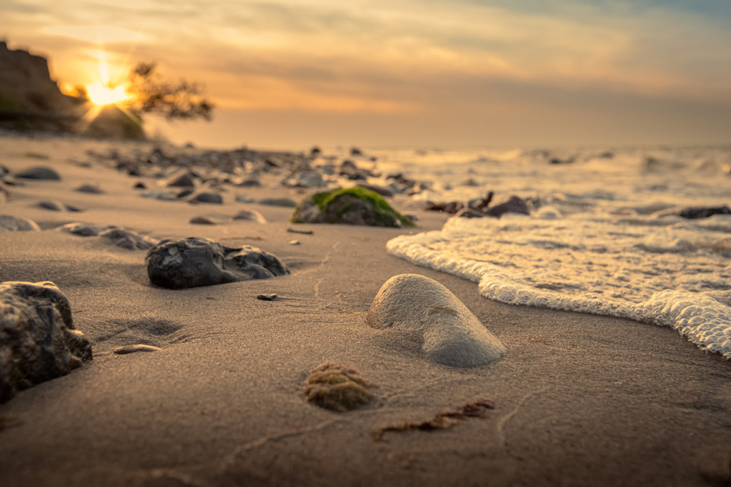 Sonnenuntergang am Strand | Das Bild zeigt einen atemberaubenden Sonnenuntergang an einem Strand an der Steilküste in Stohl. Im Vordergrund breitet sich ein langer Strand aus, der von vereinzelten Steinen bedeckt wird. Die Schönheit der Natur in Verbindung mit dem Anblick des Sonnenuntergangs schenkt dem Betrachter ein Gefühl von Frieden und Entspannung.