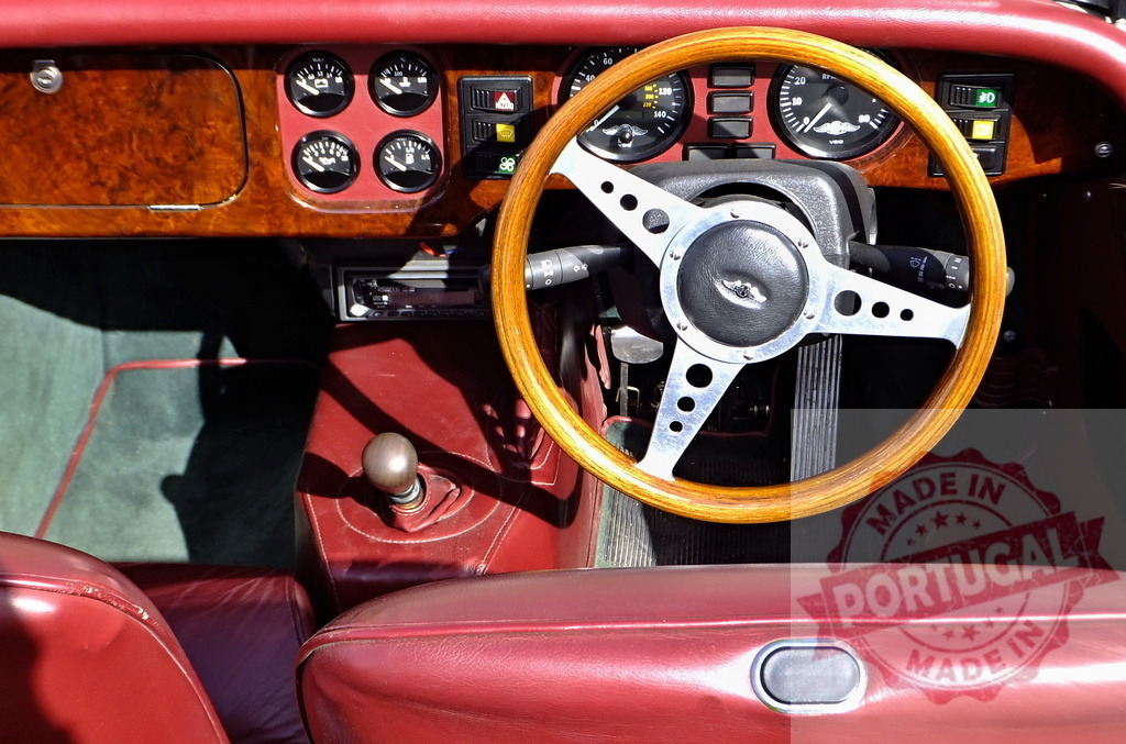Wooden steering wheel and dashboard of a vintage convertible sports car | Interior view of a classic car showing wooden dashboard, steering wheel, gear stick and red leather seats - Realized with Pictrs.com