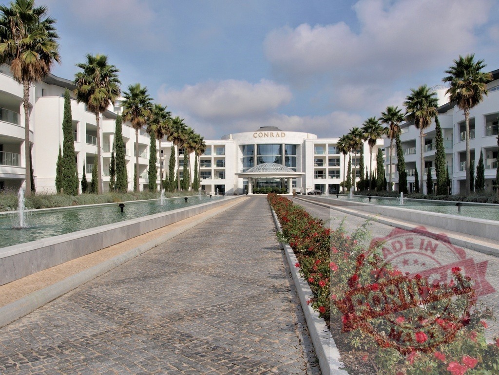 Conrad Algarve luxury resort entrance with palm trees | Conrad Algarve luxury hotel entrance driveway with fountains, water feature, and red flowers - Realized with Pictrs.com