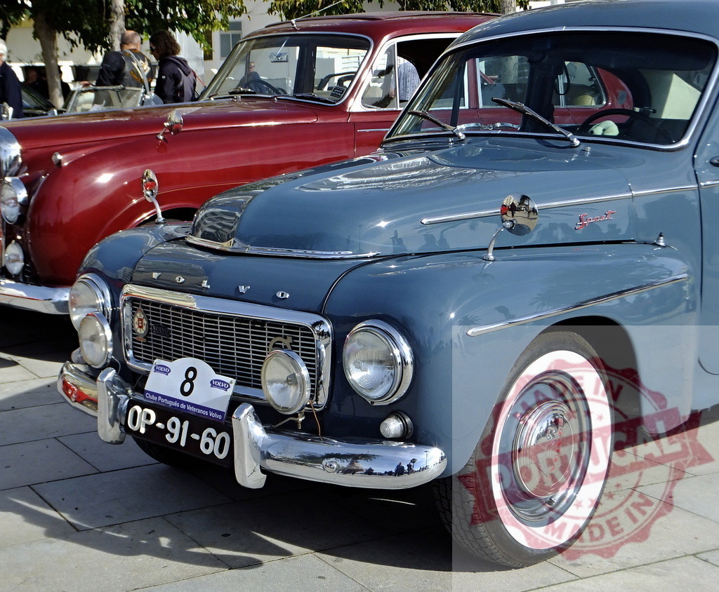Classic light blue Volvo PV544 parked near red vintage car | Shiny light blue Volvo PV544 parked on a paved surface next to a red vintage car, with onlookers in the background - Realized with Pictrs.com