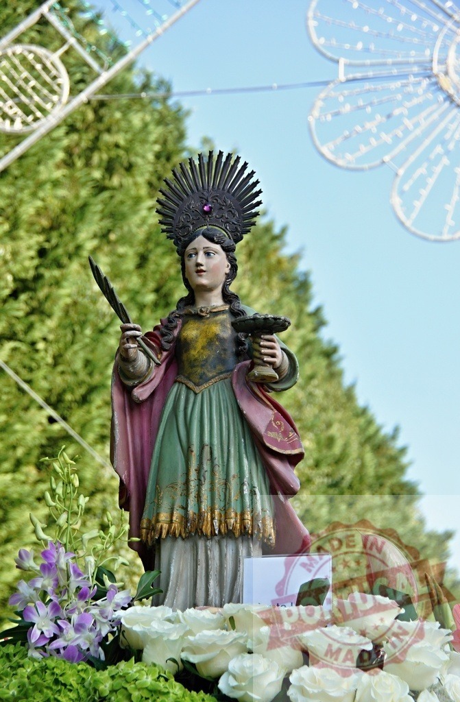 Statue of Saint Barbara holding palm branch and chalice during religious celebration | Procession 15.08.2025 - Assumption Day - Paco de Sousa, Portugal Statue of Saint Barbara holding palm branch and chalice surrounded by flowers during a religious celebration - Realisiert mit Pictrs.com