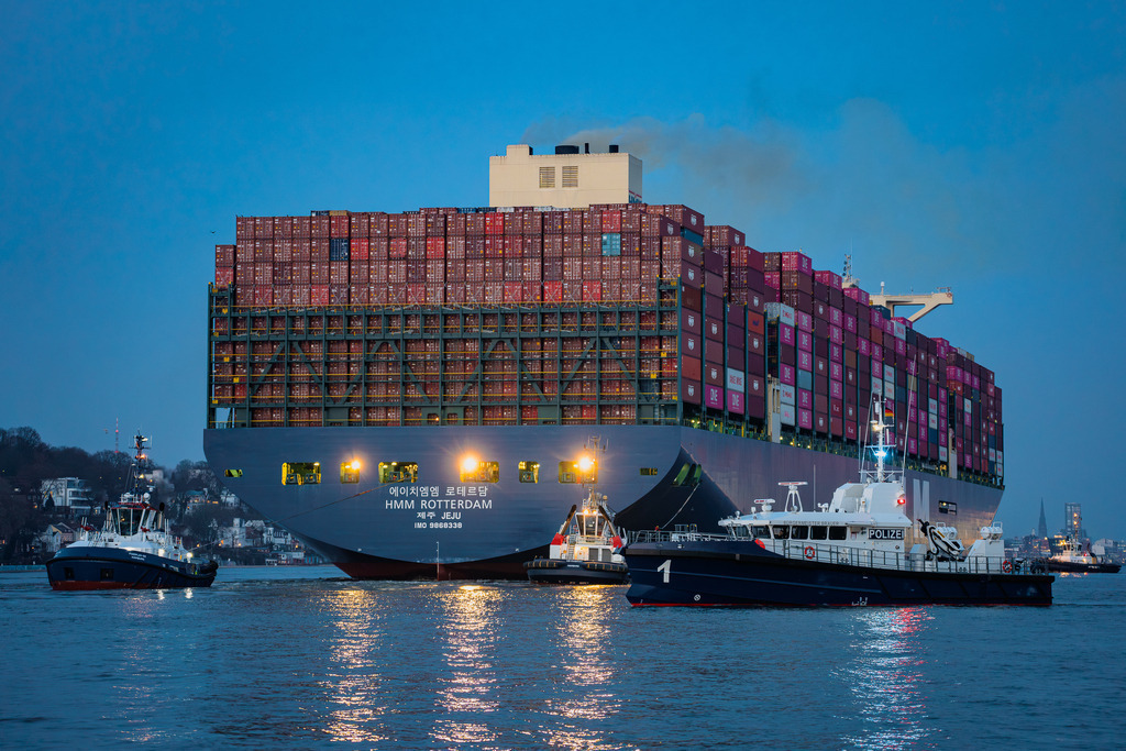 Präzisionsarbeit im Hamburger Hafen | Das Containerschiff HMM Rotterdam beim Einlaufen in den Hamburger Hafen. Die Aufnahme zeigt die Koordination zwischen den drei Assistenzschleppern und dem Boot der Wasserschutzpolizei, das das Manöver absichert. - Realisiert mit Pictrs.com