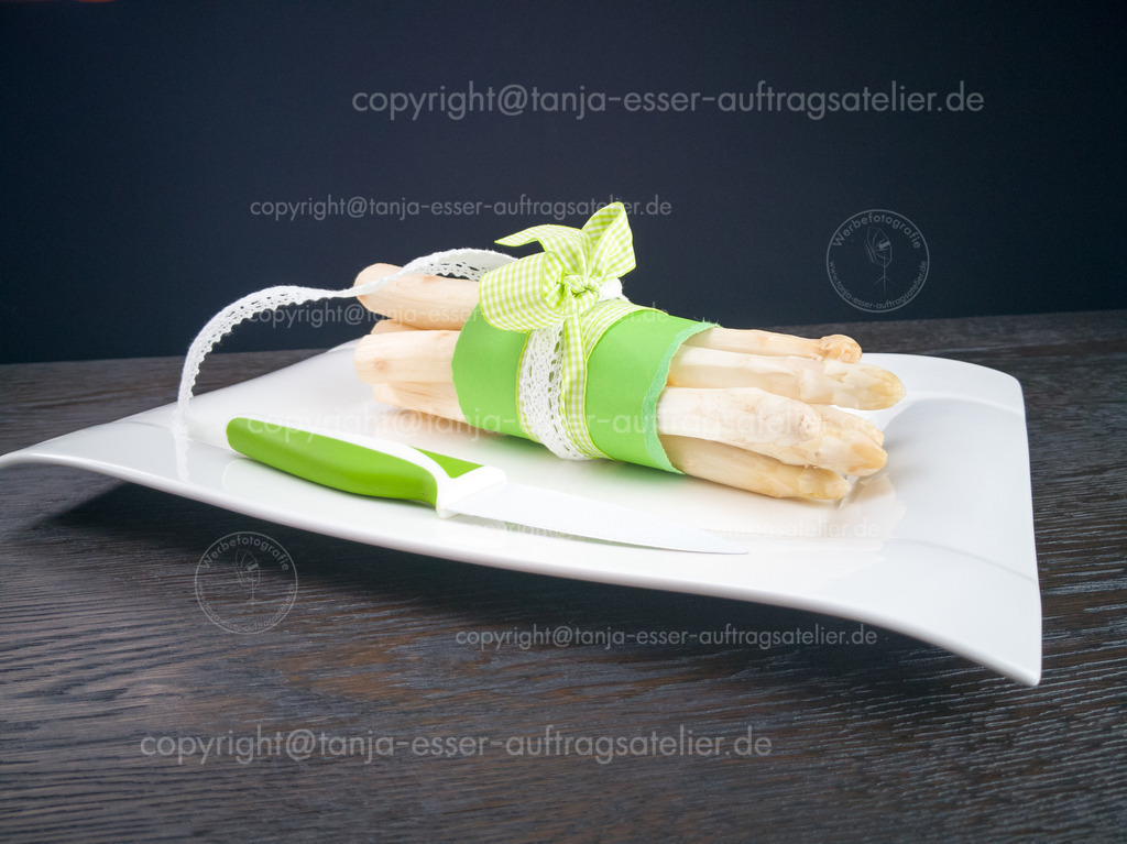 Weisser Spargel 1 D | Weißer Spargel mit grüner hübscher Schleife auf schwarzem Holztisch. Ein Kreramikmesser im gleichen grün sorgt für frische Farben.	