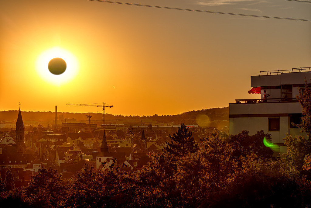 Sonnenfinsternis über Stuttgart, orangerotes Dämmerlicht | Das Bild zeigt die eindrucksvolle partielle Sonnenfinsternis vom 12. August 2026 im Abendlicht. Kurz vor dem Sonnenuntergang schob sich der Mond von Deutschland aus gesehen zu rund 85 bis 90 Prozent vor die Sonnenscheibe.Das Himmelsereignis: Am Abend des 12. August 2026 erlebte Mitteleuropa eine der stärksten partiellen Sonnenfinsternisse der letzten Jahre kurz vor Sonnenuntergang.Sichtbarkeit in der Region: Im Südwesten Deutschlands und in der Stuttgarter Region war die Sonne zu etwa 89 Prozent vom Mond verdeckt, was die Landschaft in ein außergewöhnliches Dämmerungslicht tauchte - Realisiert mit Pictrs.com