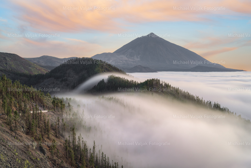 Teneriffa Mirador de Ayosa | Blick zum Teide bei einem herrlichen Sonnenuntergang. Die hoch stehenden Wolken fließen über die Hügel während die Sonne die Wolken orange färbt. Im Hintergrund hebt sich der mächtige Pico del Teide hervor, der mit 3715 m Höhe der höchste Berg Spaniens ist. - Realisiert mit Pictrs.com