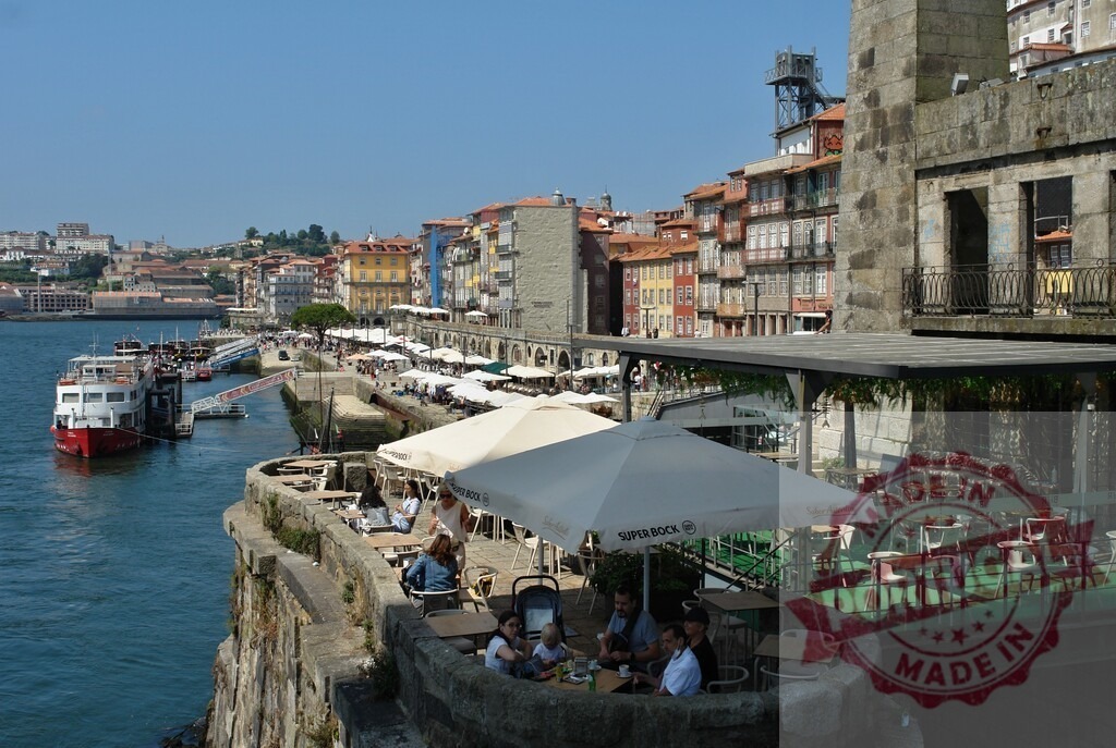 Porto Ribeira waterfront with cafes and Douro River boats. Porto - Portugal | Porto Ribeira district with crowded cafes and traditional buildings along the Douro River on a sunny day - Realized with Pictrs.com