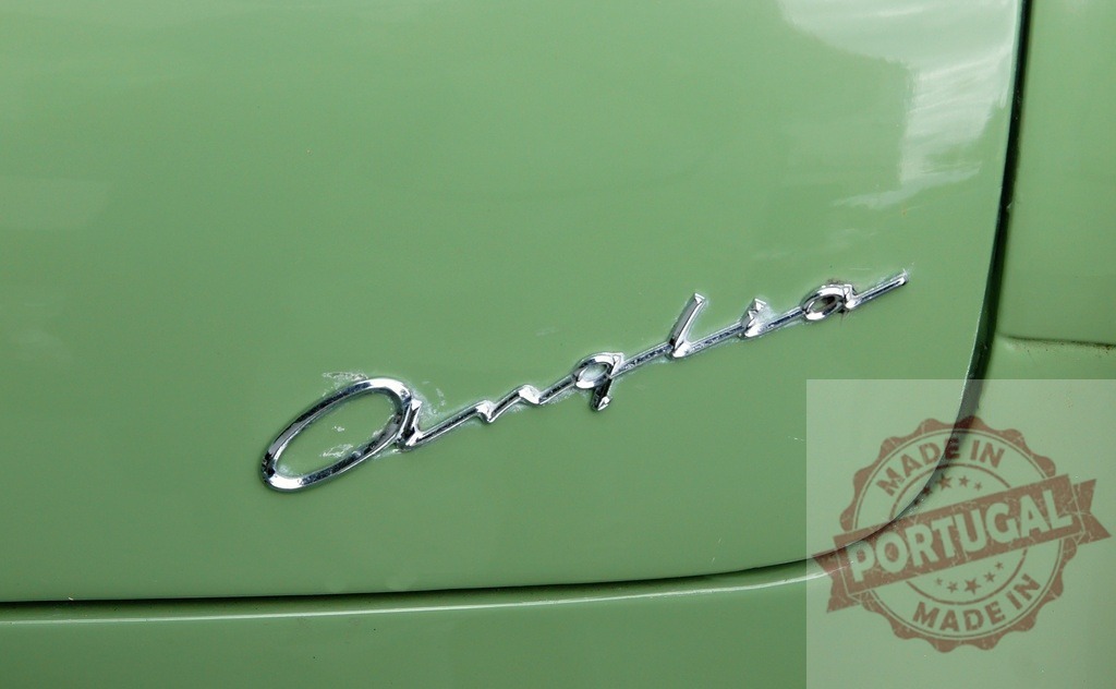 Ford Anglia vintage car chrome logo detail | Ford Anglia vintage car showcasing chrome logo on green bodywork - Realized with Pictrs.com