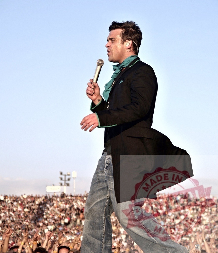 Robbie Williams holding a microphone and singing during a live concert | Robbie Williams singing on stage during a concert in front of a large audience - Realisiert mit Pictrs.com
