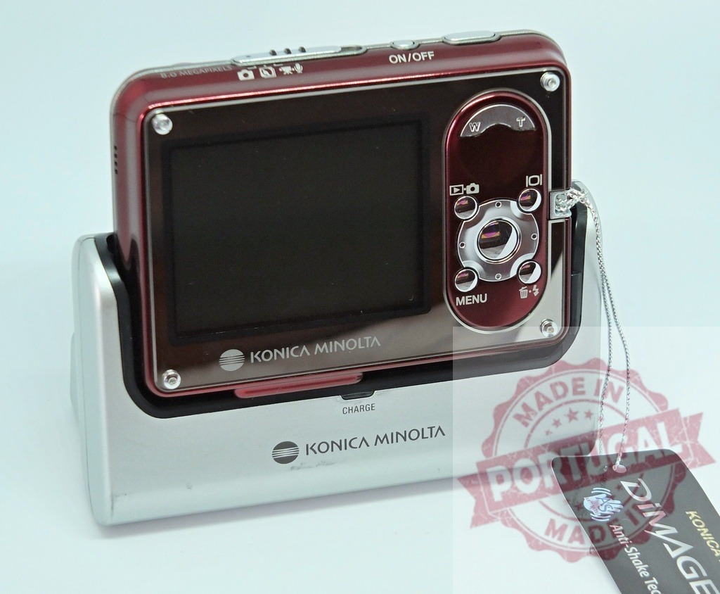 Konica Minolta DiMAGE digital camera charging on white background | Red Konica Minolta DiMAGE 8.0 megapixel digital camera charging in its dock - Realisiert mit Pictrs.com