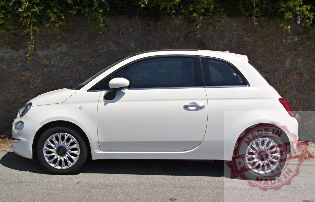 White Fiat 500 car parked on urban street | White Fiat 500 car parked side view on city street next to stone wall under green foliage - Realisiert mit Pictrs.com