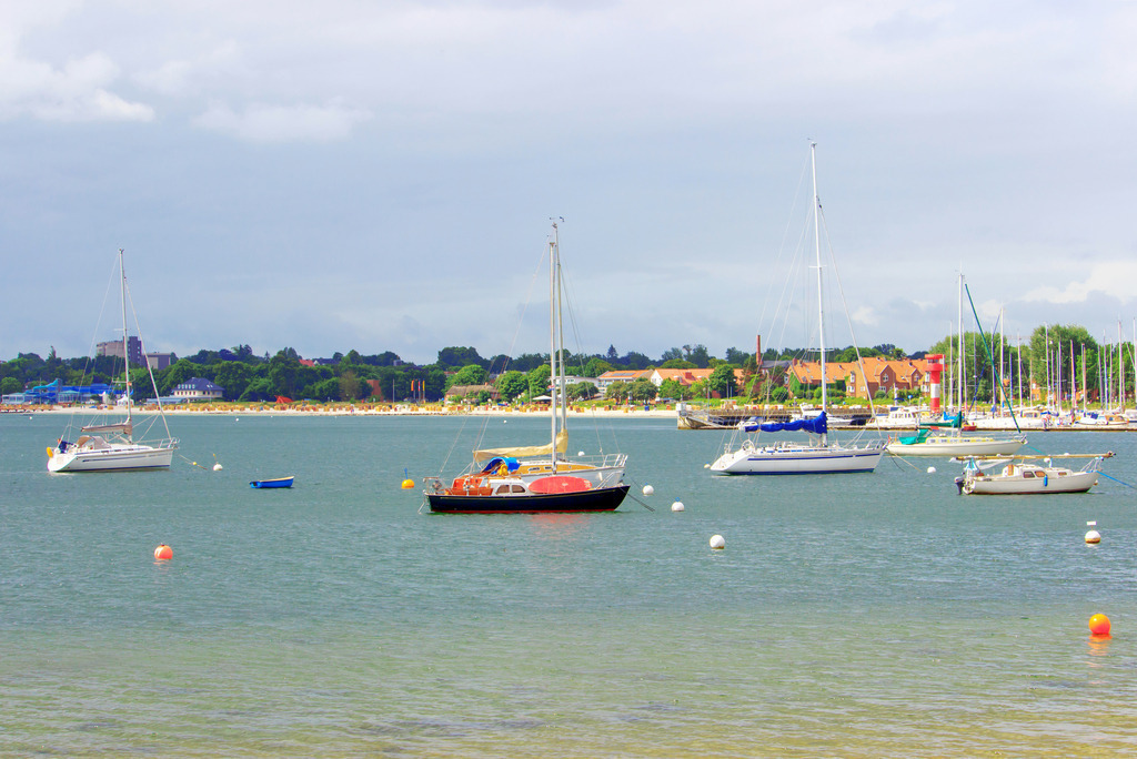 Wandbild: Segelboot vor Eckernförde   | Dieses Wandbild im Querformat zeigt Segelboot  vor Eckernförde im Sommer. Der Himmel ist stark bewölkt. In der Ferne kann man den Sandstrand sehen.  - Realisiert mit Pictrs.com