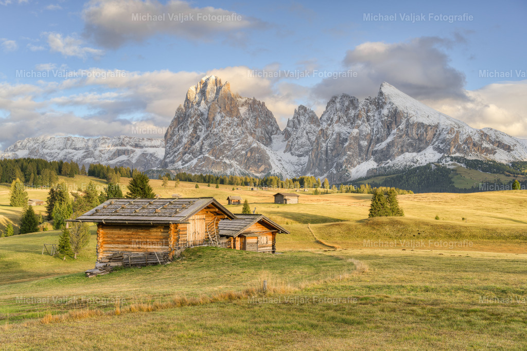 Die Seiser Alm im goldenen Licht | Blick über die Almwiesen und Almhütten der Seiser Alm in Südtirol zu den bereits mit Schnee bedeckten Bergen Langkofel und Plattkofel. Die Sonne taucht die Landschaft in ein warmes Licht. - Realisiert mit Pictrs.com