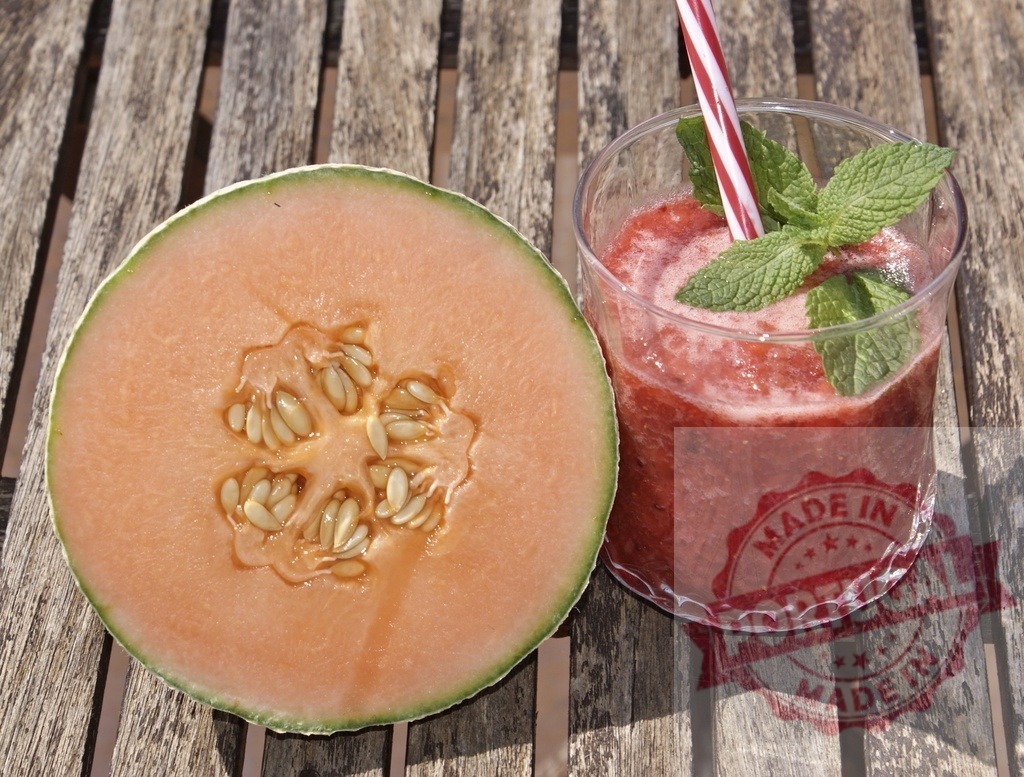 Cantaloupe melon half and refreshing strawberry smoothie | Cantaloupe melon half next to a strawberry smoothie with mint on wooden table - Realized with Pictrs.com