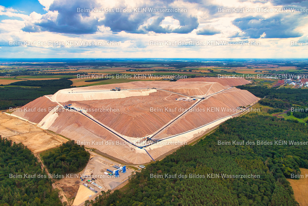 Kalimandscharo_Zielitz_Kalihalde_7352 | Das Luftbild zeigt den Kalimandscharo bei Zielitz aus einer Drohnenperspektive. Die schneeweiße, rötliche Kalihalde wirkt aus der Luft nahezu geometrisch und hebt sich mit ihren klaren Kanten und regelmäßigen Böschungen deutlich von der umgebenden Landschaft ab. Die außergewöhnliche Form macht die Halde zu einem markanten technischen Bauwerk, das schon aus großer Entfernung sichtbar ist.Der Kalimandscharo ist die Rückstandshalde des Kaliwerks Zielitz, des größten Kalibergwerks Deutschlands. Die Halde erreicht eine Höhe von rund 120 Metern über dem umliegenden Gelände beziehungsweise etwa 200 Meter über dem Meeresspiegel und besitzt eine Grundfläche von rund 110 Hektar. Sie entsteht durch die Ablagerung von Rückständen aus der Kaliproduktion, bei der jährlich rund 12 Millionen Tonnen Rohsalz gefördert und verarbeitet werden.Die Drohnenaufnahme verdeutlicht eindrucksvoll die nahezu geometrische Form der Halde und ihre technischen Dimensionen. Das Luftbild dokumentiert eines der markantesten Zeugnisse des Kalibergbaus in Deutschland und zeigt, wie moderne Rohstoffgewinnung das Landschaftsbild nachhaltig prägt. - Realisiert mit Pictrs.com