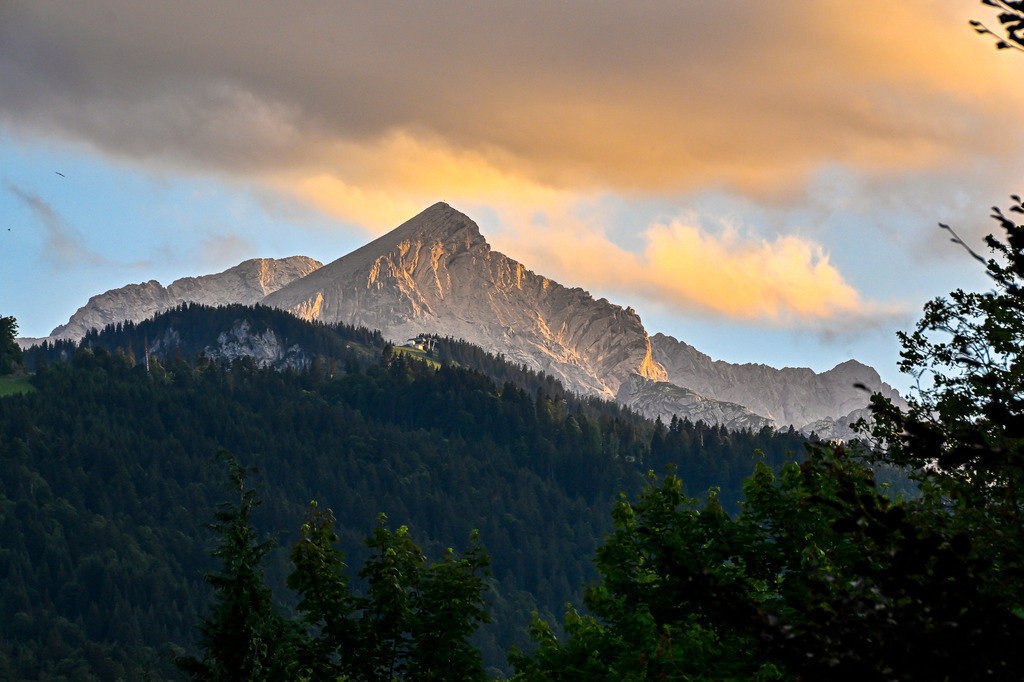 Das goldene Herz des Werdenfelser Landes | Ein majestätischer Blick auf die Alpspitze im imposanten Zugspitzmassiv nahe Garmisch-Partenkirchen: Kraftvoll bricht der markante Gipfel durch das dichte Grün der bewaldeten Hänge und streckt sich dem Himmel entgegen. Es ist die magische Stunde des Sonnenuntergangs, in der die Natur tief durchatmet. Die untergehende Sonne taucht die schroffen Kalksteinfelsen in ein warmes, goldenes Licht, das einen faszinierenden Kontrast zu den kühlen Schatten des Tals bildet. Ein Bild voller erhabener Ruhe, das die Sehnsucht nach der rauen Schönheit der bayerischen Alpen weckt. - Realisiert mit Pictrs.com