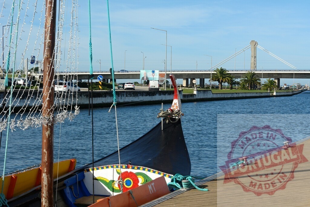 Moliceiro boat moored on an Aveiro canal with bridge | Traditional Moliceiro boat tied to a dock, showing a decorated prow with a modern bridge in the background - Realisiert mit Pictrs.com