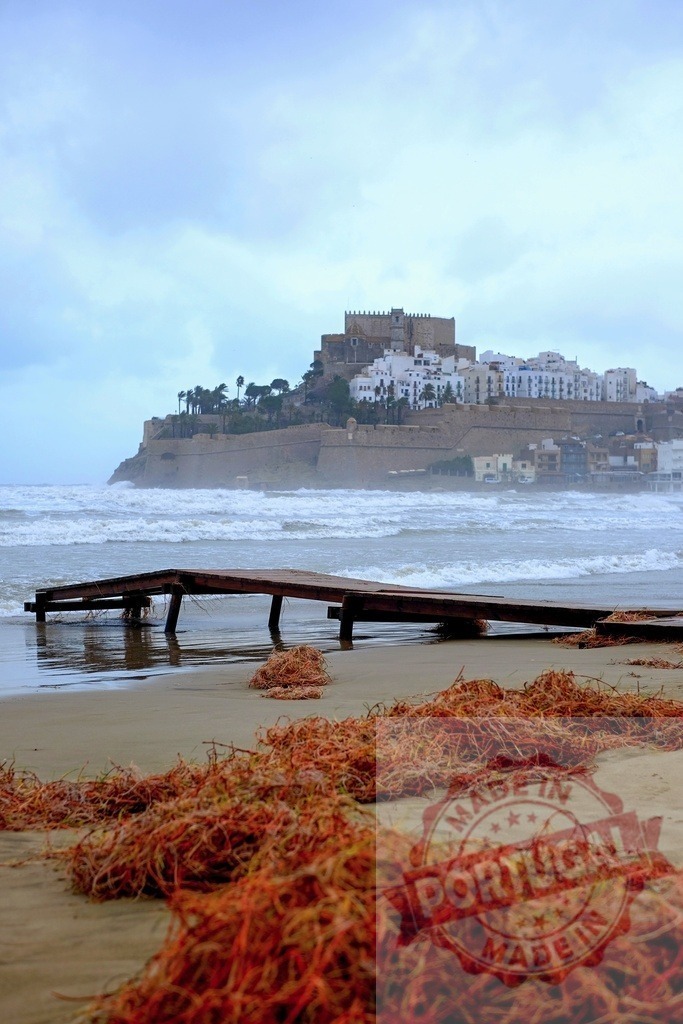 Peniscola Castle dominating the skyline over rough sea and orange seaweed on beach | Peniscola Castle towering over stormy sea with orange seaweed washed ashore on beach - Realisiert mit Pictrs.com