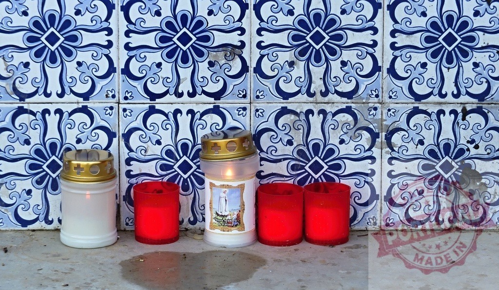 Votive candles burning against azulejo wall in Portugal | Votive candles burning for faith and prayer against traditional Portuguese azulejo tiles - Realized with Pictrs.com