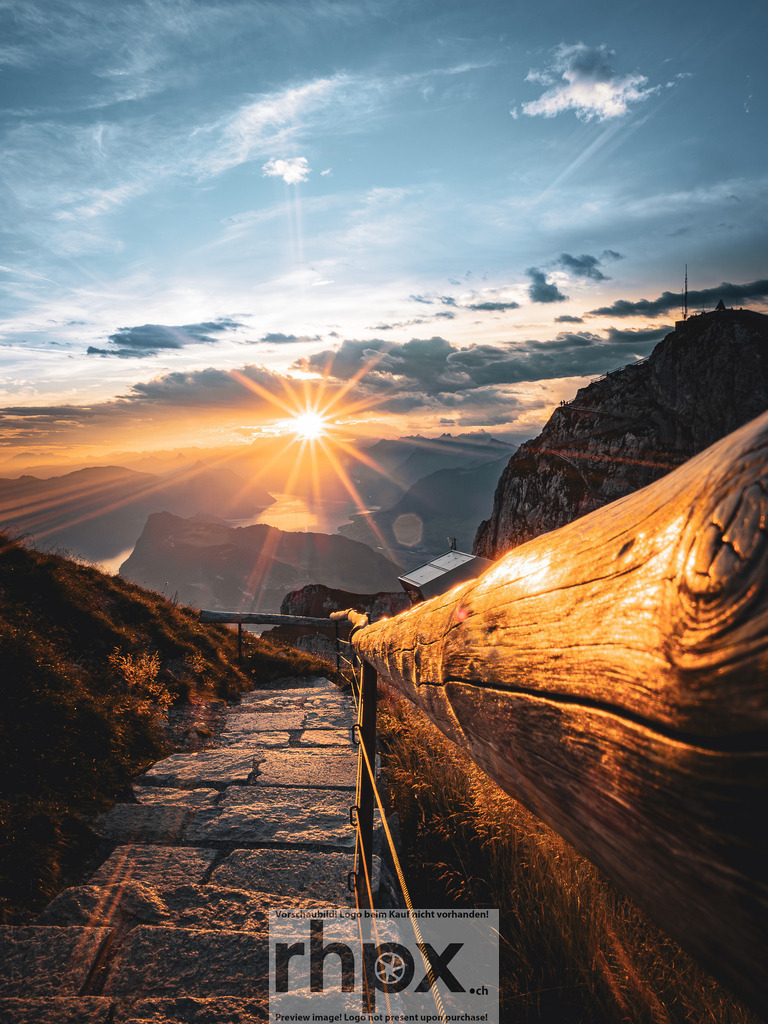 Goldener Gratweg Pilatus | Abendgold. Holz. Horizont.Die letzten Strahlen der untergehenden Sonne tauchen den steinernen Bergpfad und das verwitterte Holz in ein warmes, spektakuläres Licht. Ein Moment der absoluten Ruhe, in dem der Blick über die Gipfel und den glitzernden See bis in die unendliche Ferne schweift.Wähle unter "Produktauswahl" dein Wunschformat: Vom klassischen Wandbild über Puzzle &amp; Tassen bis zum digitalen Download (z.B. als Handy-Hintergrund). - Realisiert mit Pictrs.com