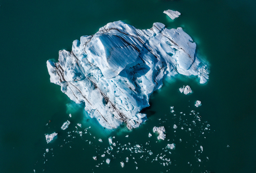 island-DJI_0560 | Jökulsárlón ist eine Gletscherlagune, die an den Nationalpark Vatnajökull im Südosten Islands angrenzt. Im Wasser schwimmen unzählige Eisberge des Vatnajökull-Gletschers. Einige Eisberge sind leuchtend blau, andere - wie dieser - besitzen graue Streifen von den Ascherückständen früherer Vulkanausbrüche. - Realisiert mit Pictrs.com