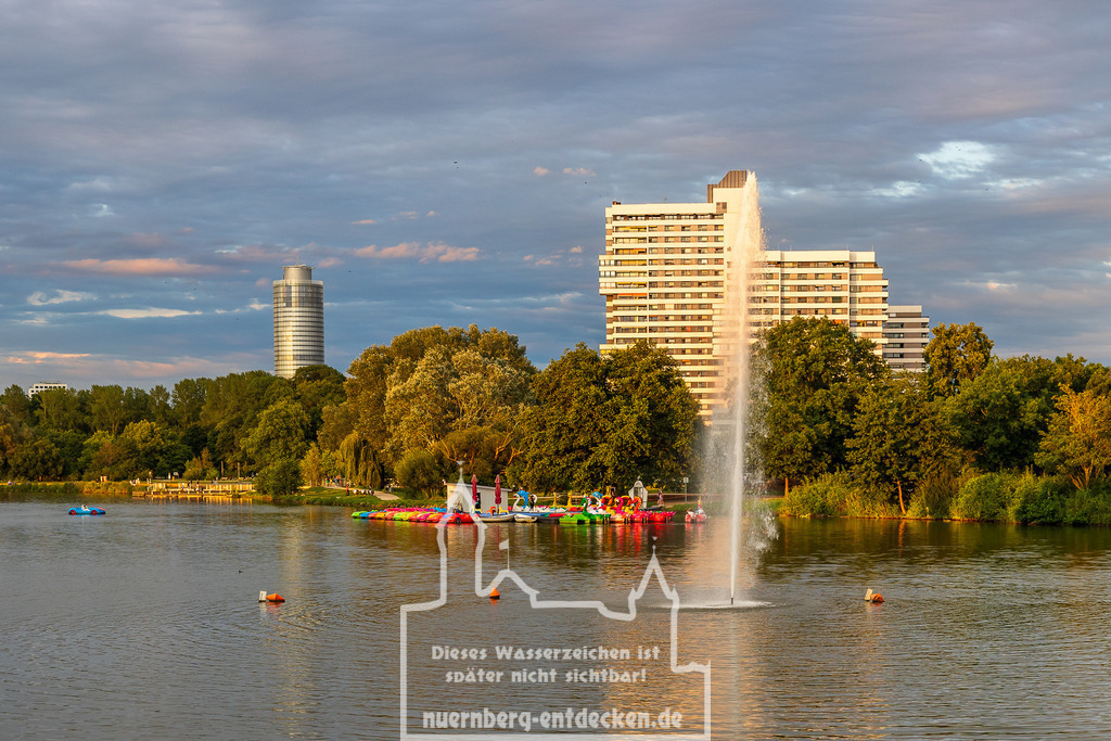 Monatsbild des Kalender 2025 für den Monat Mai | Der Wöhrder See in Nürnberg an einem Sommerabend: Im Hintergrund erheben sich der markante Business Tower und das Wohnhaus Norikus. Im Vordergrund scha0ukeln zahlreiche bunte Tretboote sanft auf dem Wasser. - Realisiert mit Pictrs.com