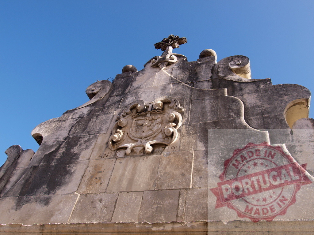 Baroque stone church facade with crest and cross against blue sky | Ornate baroque stone church facade featuring a historical crest, cross, and weathered details under a clear sky - Realized with Pictrs.com