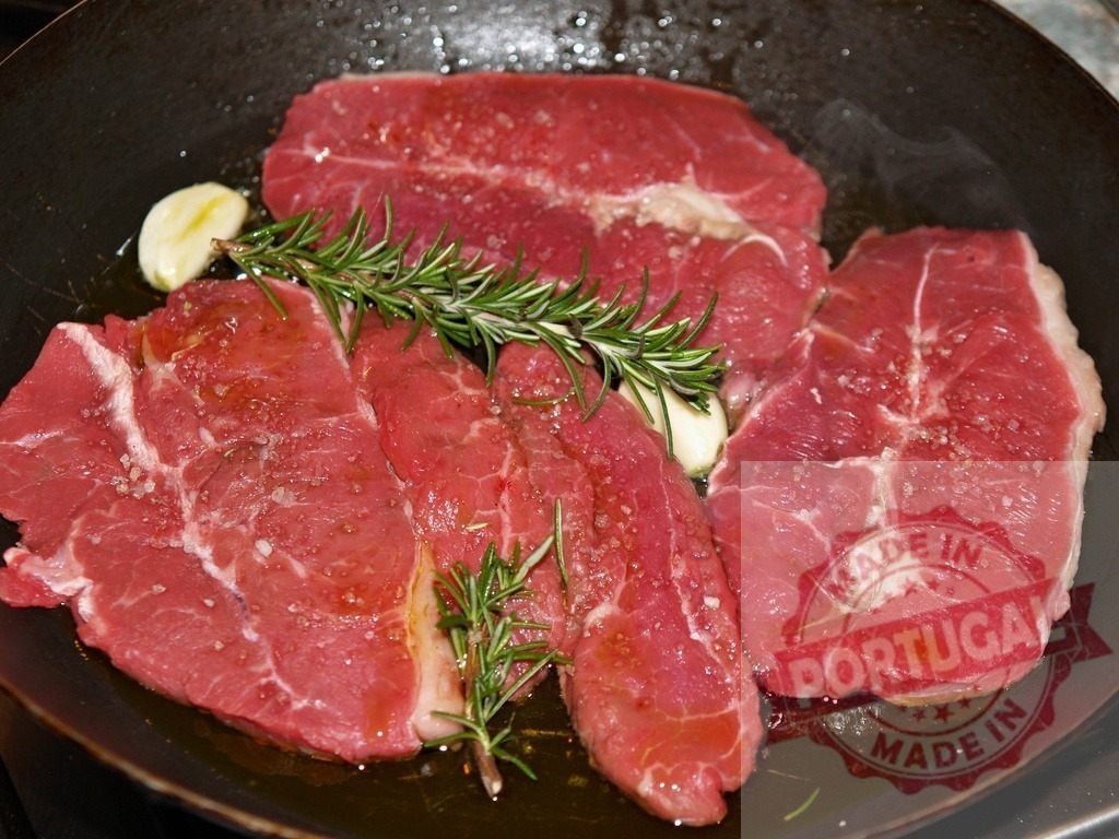 Raw beef steaks frying in pan with rosemary and garlic | Raw beef steaks cooking in a pan with rosemary, garlic, and seasoning - Realized with Pictrs.com
