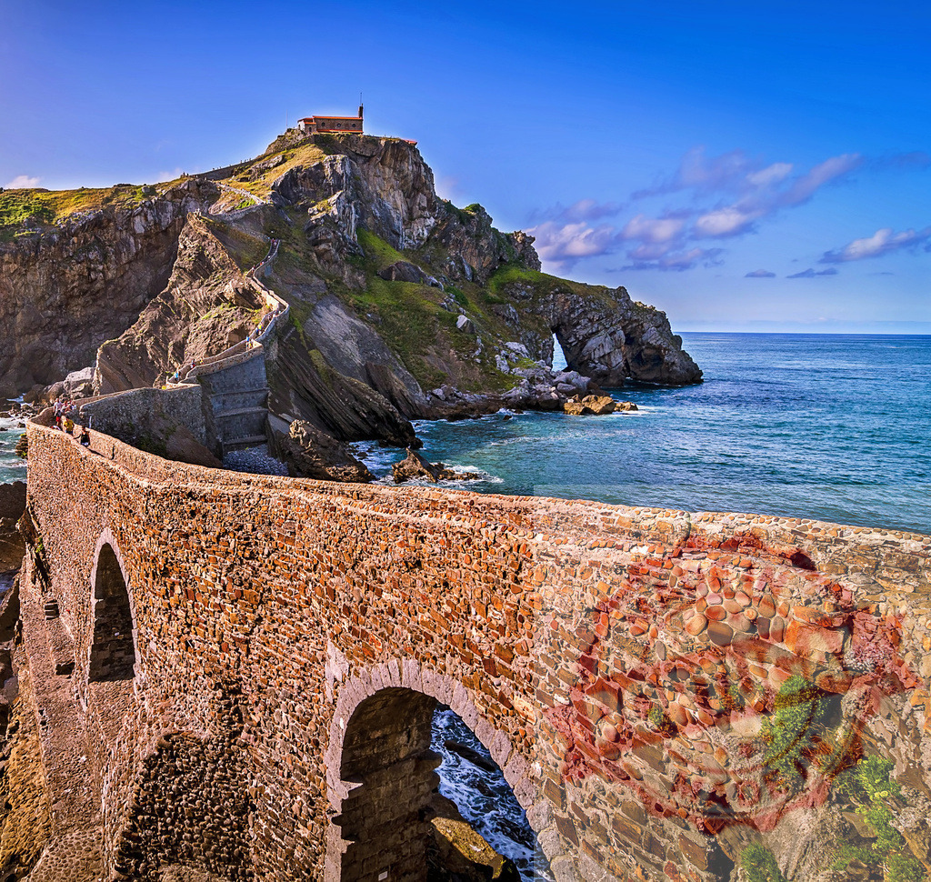 Gaztelugatxe hermitage overlooking stone bridge and coast of Biscay | Stone bridge leading to San Juan de Gaztelugatxe hermitage on a sunny day in Basque Country - Realized with Pictrs.com