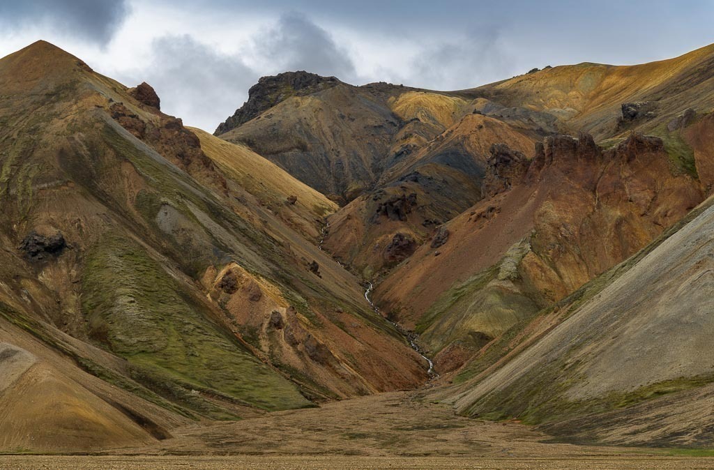 island-2019-223 | Rhyolith ist das vulkanische Gestein der Bergwelt in Landmannalaugar. Andere geologische Elemente wie Schwefel, Eisen und Moos färben die Hänge in vielfältige Töne aus Braun, Gelb, Rosa, Rot und Blau. Landmannalaugar wurde deshalb einmal als „eine Oase inmitten einer urweltlichen Landschaft“ bezeichnet. - Realisiert mit Pictrs.com