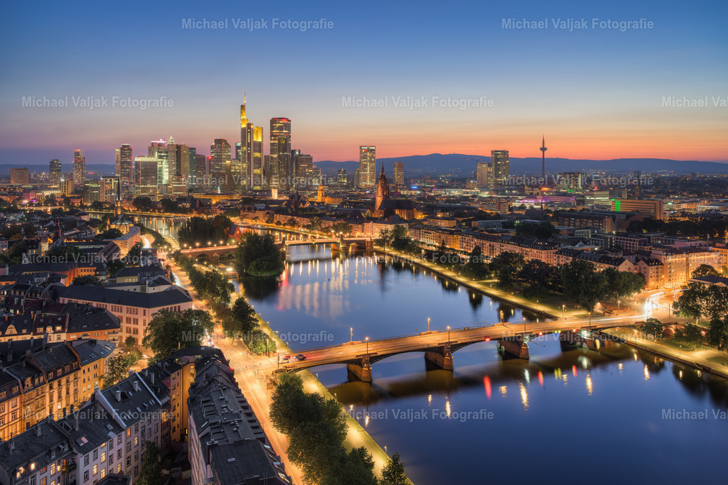 Frankfurt Blick über den Main zur Skyline am Abend | Der Blick über den Main auf die Frankfurter Skyline kurz nach Sonnenuntergang zeigt die Stadt in einem ruhigen, geordneten Moment. Die Hochhäuser sind bereits beleuchtet, der Himmel ist noch leicht gefärbt vom Restlicht des Tages. Die Spiegelungen im Wasser verstärken die Symmetrie und geben dem Bild Tiefe.Es ist eine Szene ohne große Dramatik – aber gerade das macht ihren Reiz aus. Die Architektur tritt in den Vordergrund, klar umrissen und ohne Ablenkung. Der Fluss wirkt wie eine natürliche Grenze zwischen Bewegung und Ruhe, zwischen Stadt und Perspektive.Frankfurt präsentiert sich hier als moderne, funktionale Stadt mit einer markanten Silhouette. Kein überhöhter Moment, sondern ein realistischer, unaufgeregter Blick auf den urbanen Alltag am Abend. Wer sich für Stadtlandschaften interessiert, findet in diesem Bild eine klare, reduzierte Ästhetik. - Realisiert mit Pictrs.com