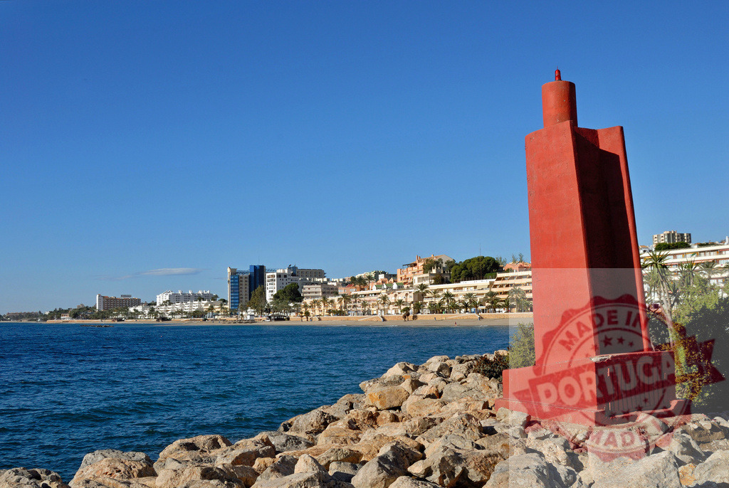 Lighthouse on rocky coast with Marbella cityscape | Red lighthouse standing on coastline with calm sea and buildings along the beach - Realisiert mit Pictrs.com