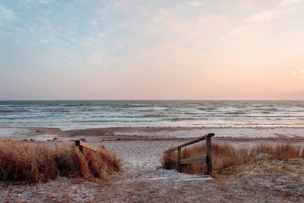 Wandbild: Treppe an den Sandstrand im Morgenrot | Dieses Wandbild im Querformat zeigt eine Treppe, die an den Strand führt im Morgenrot. Auf der linken und rechten Seite der Treppe wachst Strandgras. Der Himmel leuchtet in einem Verlauf von blau bis rotorange. Auf dem Meer sind zahlreiche Wellen zu sehen, die an den Strand rauschen. Ein Wandbild, welches zum Träumen einlädt. Holen Sie sich diese schöne maritime Morgenstimmung auf Leinwand, Aluminium-Platte oder als Glasbild. Ideal fürs Wohnzimmer, Schlafzimmer, Küche, den Arbeitsplatz oder die Ferienwohnung. Die Wandbilder werden individuell für Sie in vielen Abmessungen produziert. - Realisiert mit Pictrs.com