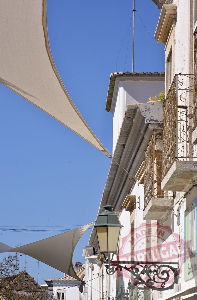 Tavira street scene with shade sails and lamppost | White buildings lining a sunny street in Tavira, Portugal, with decorative lamppost and shade sails - Realisiert mit Pictrs.com