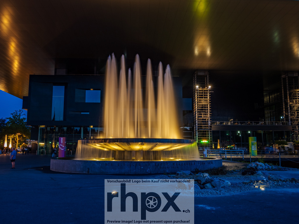 Wagenbach-Brunnen am KKL | Wasser. Licht. Eleganz.
Die illuminierten Wasserfontänen des Wagenbach-Brunnens steigen vor der modernen Kulisse des KKL in den Abendhimmel empor. Die goldene Beleuchtung kontrastiert sanft mit dem kühlen Blau der Dämmerung und schafft eine fast meditative Dynamik.
Wähle unter "Produktauswahl" dein Wunschformat: Vom klassischen Wandbild über Puzzle &amp; Tassen bis zum digitalen Download (z.B. als Handy-Hintergrund).
 - Realisiert mit Pictrs.com