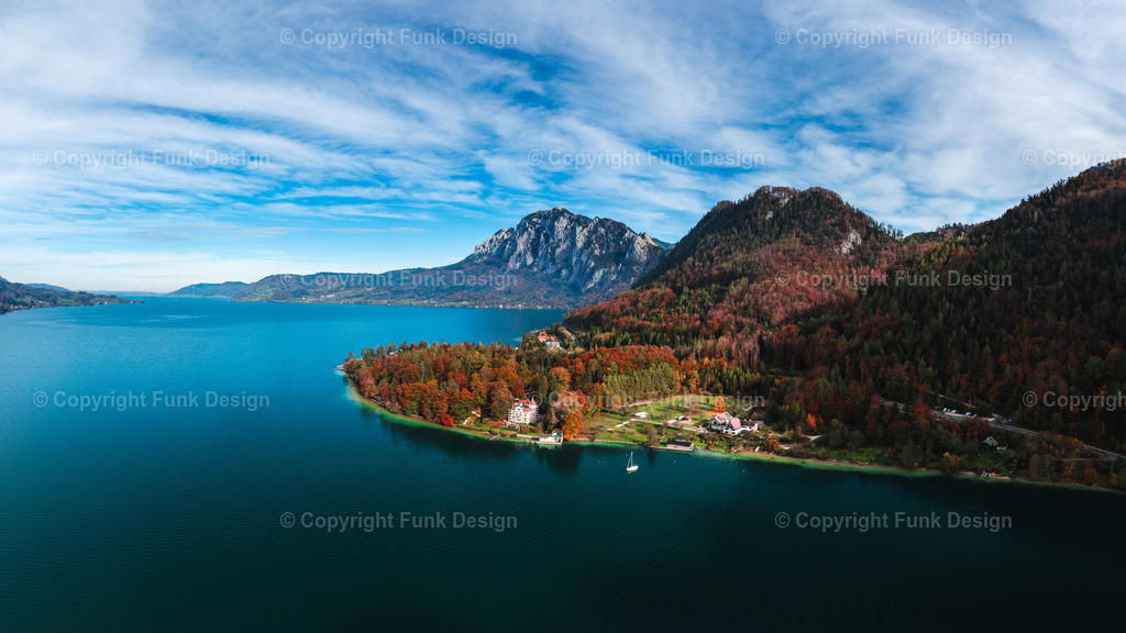 Drohnenpanorama vom Attersee im Herbst – Oberösterreich, Österreich | Ein ruhiges Drohnenpanorama zeigt den Attersee im Herbst: tiefblaues Wasser, bunt gefärbte Wälder am Ufer und eine markante Bergkulisse im Hintergrund. Das kleine Segelboot setzt einen feinen Akzent und macht die Szene besonders leicht und frei.